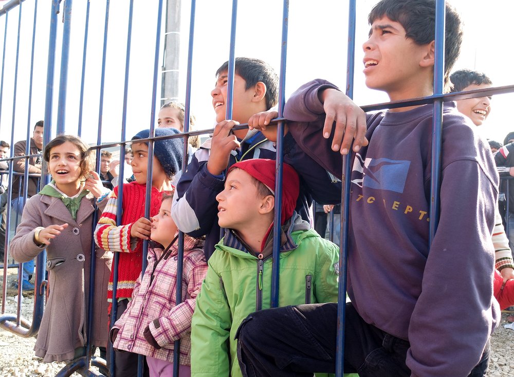 Flüchtlingskinder im kroatischen Slavonski Brod / © 2015 KNA, www.kna-bild.de - Nutzungsrechte vorbehalten., Inga Kilian Flüchtlingskinder blicken durch einen Zaun im kroatischen Transit-Camp Slavonski Brod. Freiwillige Helfer haben sich als Clowns verkleidet und versuchen, die Kinder zum Lachen zu bringen.