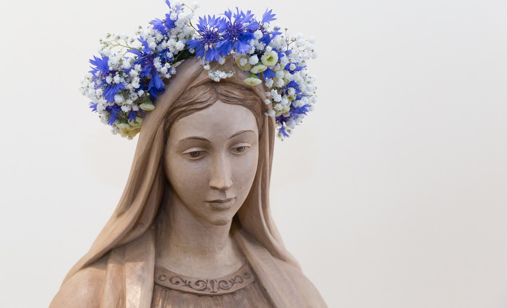 Geschnitzte Statue der Jungfrau Maria mit Blumenkranz / Radio Maria Österreich Österreichweit Andachten im Marienmonat Mai