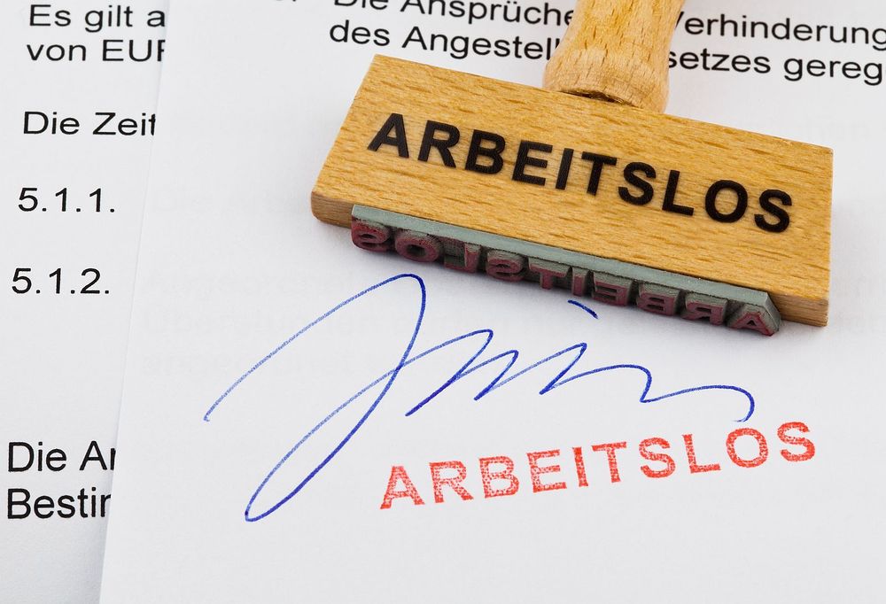 Ein Stempel aus Holz liegt auf einem Dokument. Deutsche Aufschrift: arbeitslos