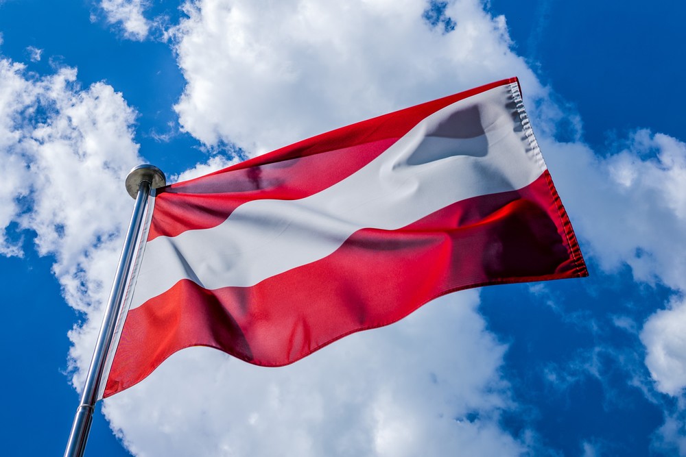 Österreich. Flagge der Republik weht vor blauem Himmel mit Wolken im Wind